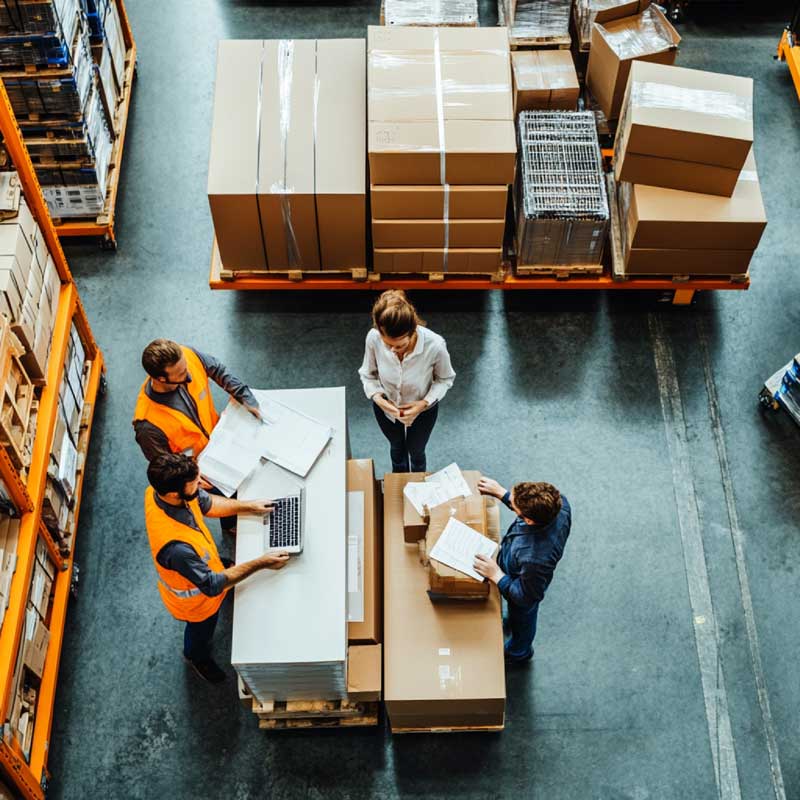 Overhead view of warehouse team reviewing documents and packages on pallets while coordinating shipments.