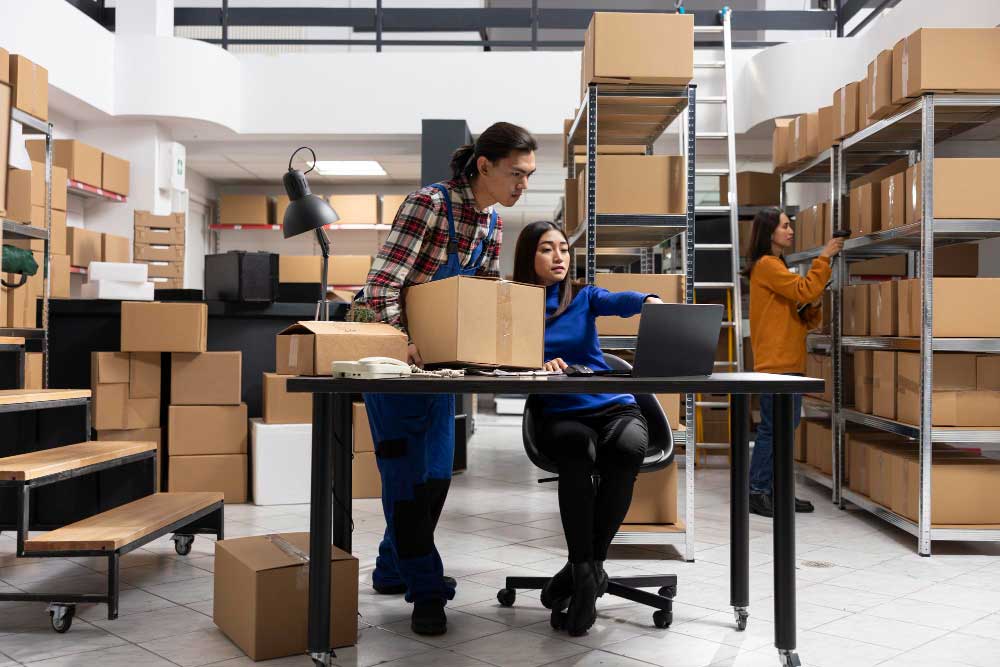 Warehouse Team Managing Order Fulfillment Warehouse staff managing inventory and processing orders using a laptop in a fulfillment center.